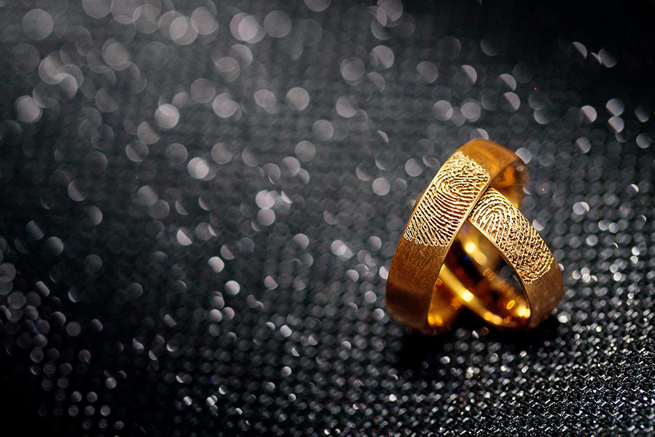 Goldene Trauringe mit Fingerabdruck auf schwarzer Clutch Goldene Trauringe mit Fingerabdruck auf schwarzer Clutch