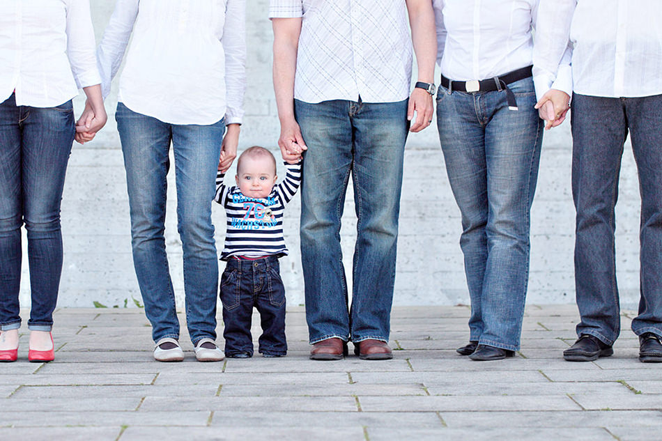 Kleinkind auf einem Familienfoto zwischen dein Beinen seiner Eltern Kleinkind auf einem Familienfoto zwischen dein Beinen seiner Eltern