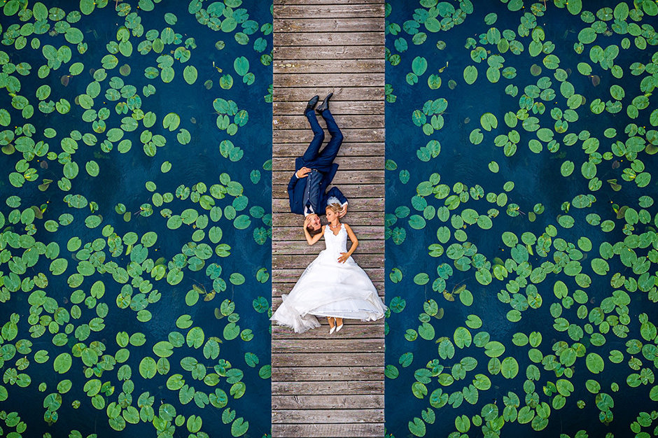 Hochzeitsfotograf nutzt Drohne am Steg Von Seerosen umgebenes Brautpaar liegt im Hochzeitsfoto auf einem Steg in Brandenburg