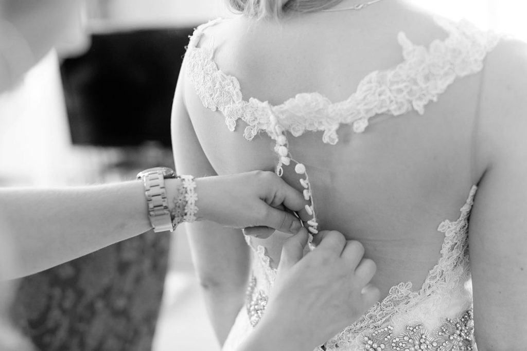 Detailfoto in schwarz weiß vom Rücken einer Braut, deren Hochzeitskleid fertig gestickt wird. Die Braut hat zwei Hochzeitsfotografen gebucht, die gleichzeitig beide Vorbereitungen fotografieren. Detailfoto in schwarz weiß vom Rücken einer Braut, deren Hochzeitskleid fertig gestickt wird. Die Braut hat zwei Hochzeitsfotografen gebucht, die gleichzeitig beide Vorbereitungen fotografieren.