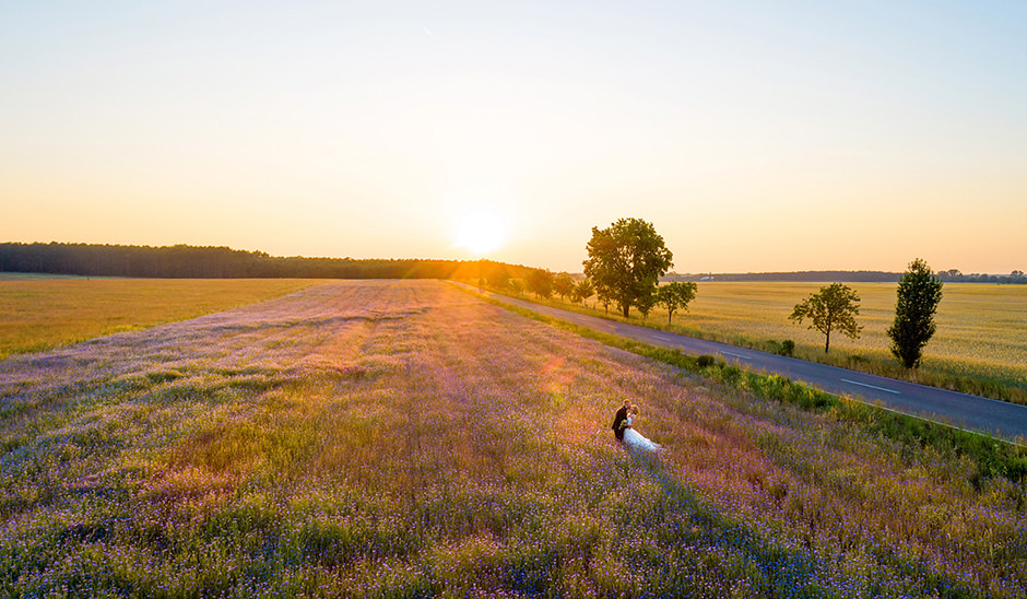 Hochzeitsfoto mit Drohne: Brautpaar im Sonnenuntergang auf Feld in Brandenburg: dramatische Beleuchtung in den Abendstunden sind bezeichnend für den Stil von den auf vielen Hochzeiten zu zweit fotografierenden professionellen Hochzeitsfotografen Reinhardt & Sommer Hochzeitsfoto mit Drohne: Brautpaar im Sonnenuntergang auf Feld in Brandenburg: dramatische Beleuchtung in den Abendstunden sind bezeichnend für den Stil von den auf vielen Hochzeiten zu zweit fotografierenden professionellen Hochzeitsfotografen Reinhardt & Sommer