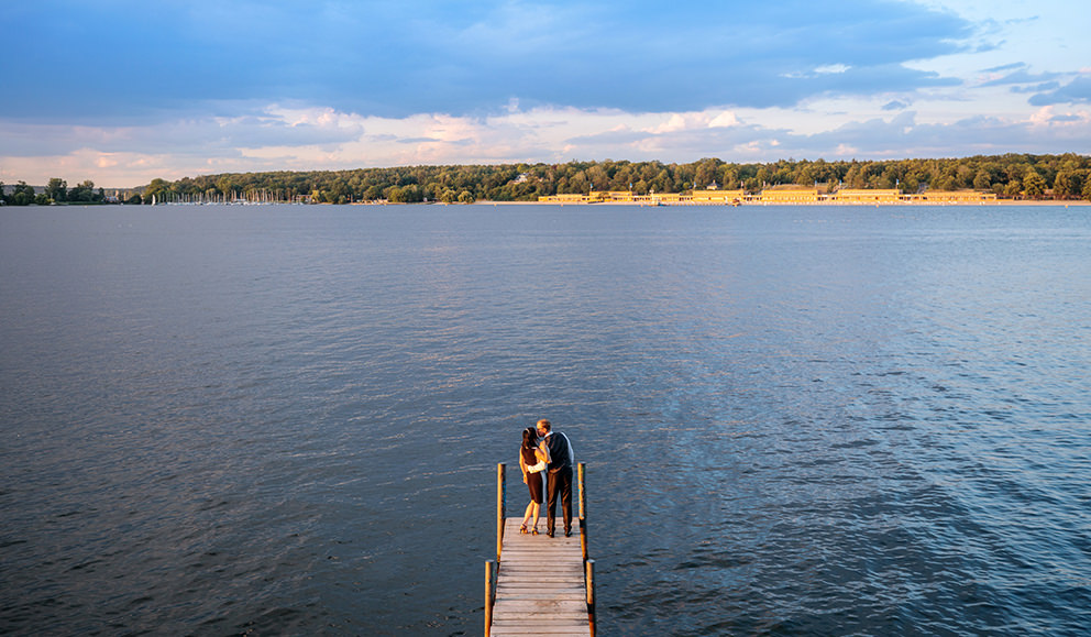 Brautpaar in Hochzeitsbildern auf Steg zur Havel mit Blick auf das Strandbad Wannsee an der Havel