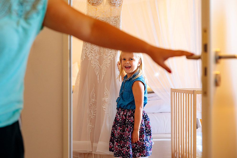 Kleines Blumenmädchen betrachtet begeistert das Brautkleid