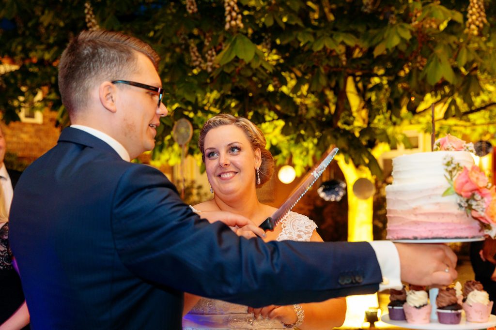 Die Braut blickt ganz verliebt ihren Bräutigam an während sie gemeinsam die Hochzeitstorte anschneiden