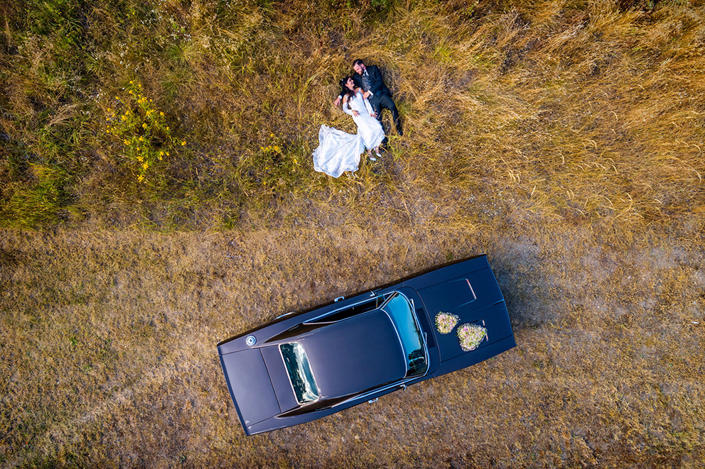 Drohnenbild mit Hochzeitsauto und Paar im Gras