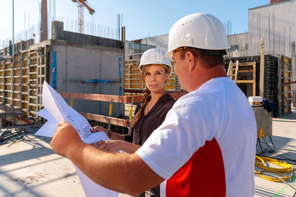 Businessfoto von Prüfingenieuren bei einem abstimmenden Blick über die Pläne auf einer Baustelle