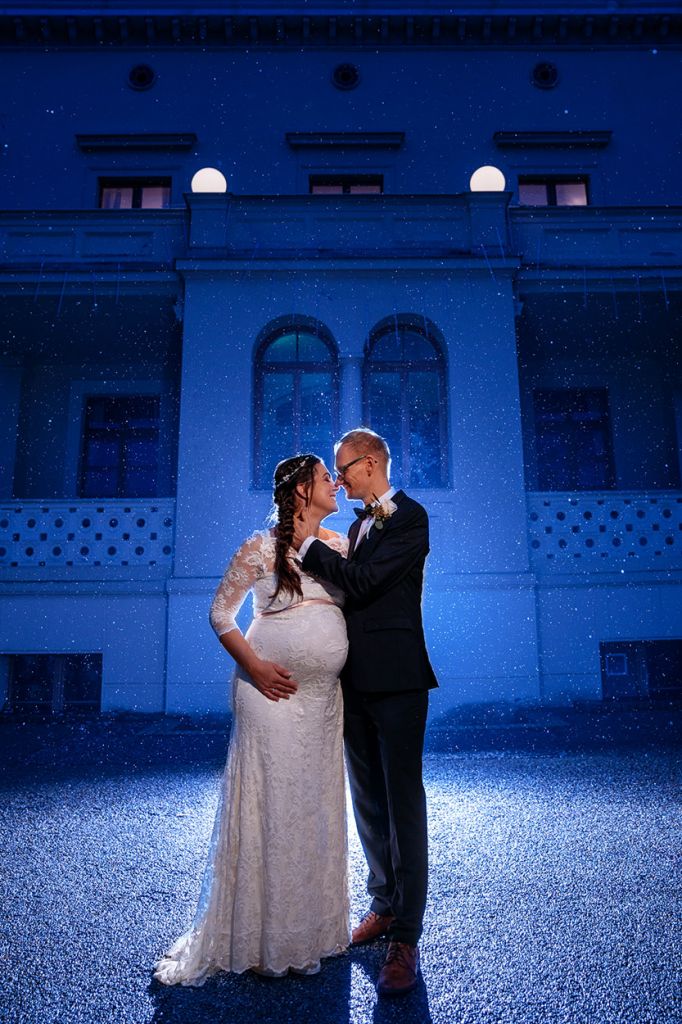 Schwangere Braut und Bräutigam im Regen bei einem Hochzeitsfoto zur blauen Stunde Schwangere Braut und Bräutigam im Regen bei einem Hochzeitsfoto zur blauen Stunde