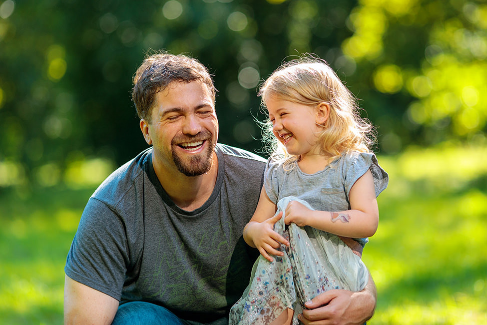 Papa und Tochter lachen herzlich auf Wiese