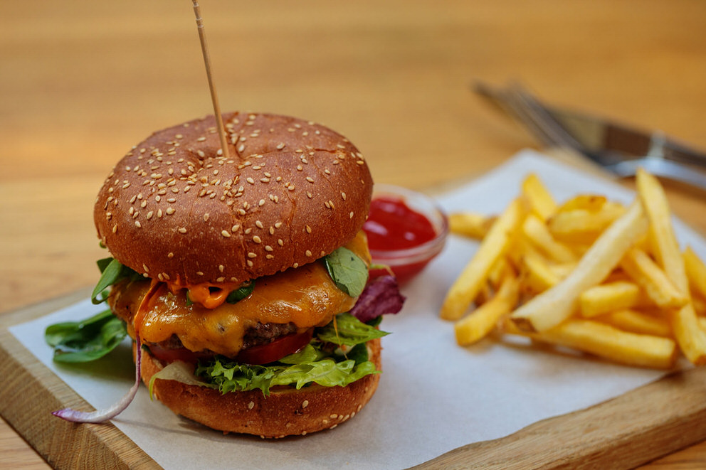 Foodfotograf: Ein Burger mit saftig am Fleisch herunterfließender Sauce mit Pommes und Ketchup serviert
