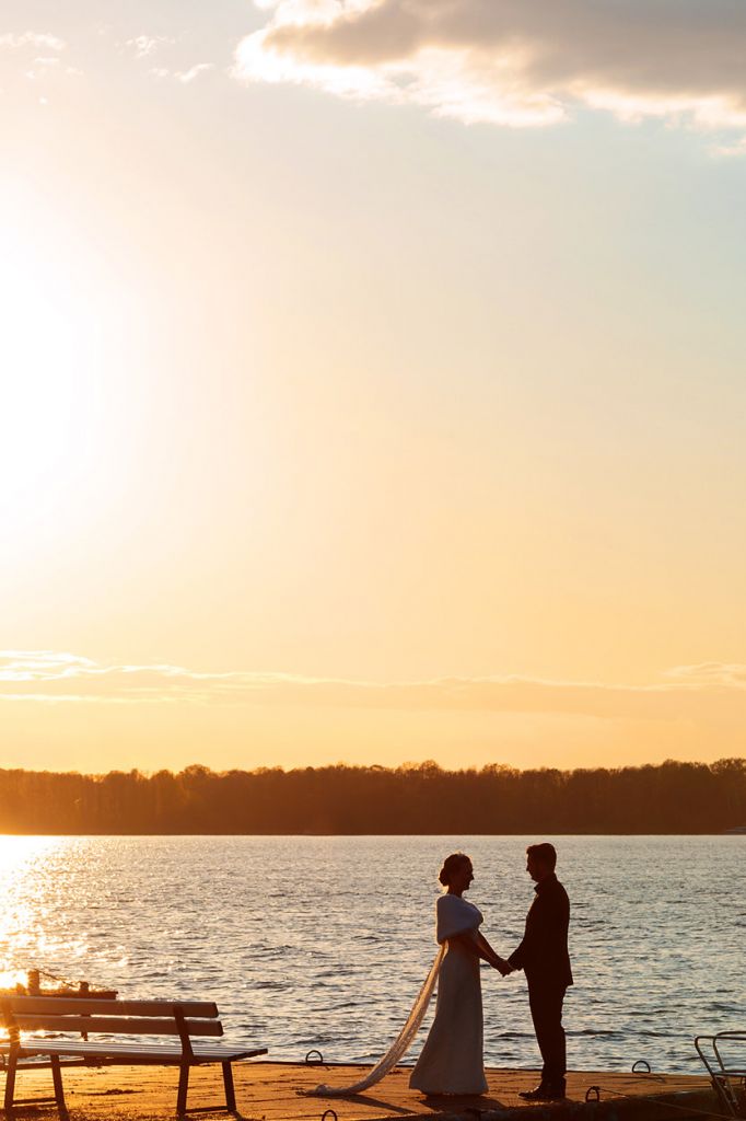 Brautpaar steht Hand in Hand am Wasser