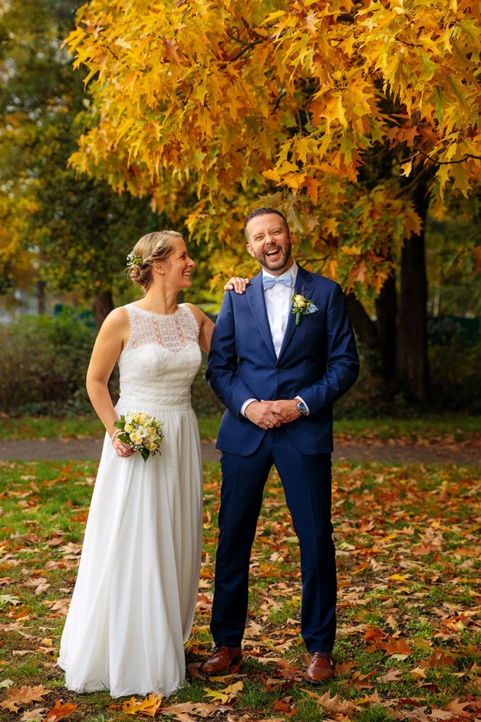 Braut und Bräutigam stehen lachend im herbstlichen Park