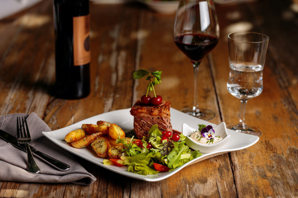 Foto von einem saftigen Steak mit Kartoffeln und Salatbeilage. Dazu ein Glas Rotwein!