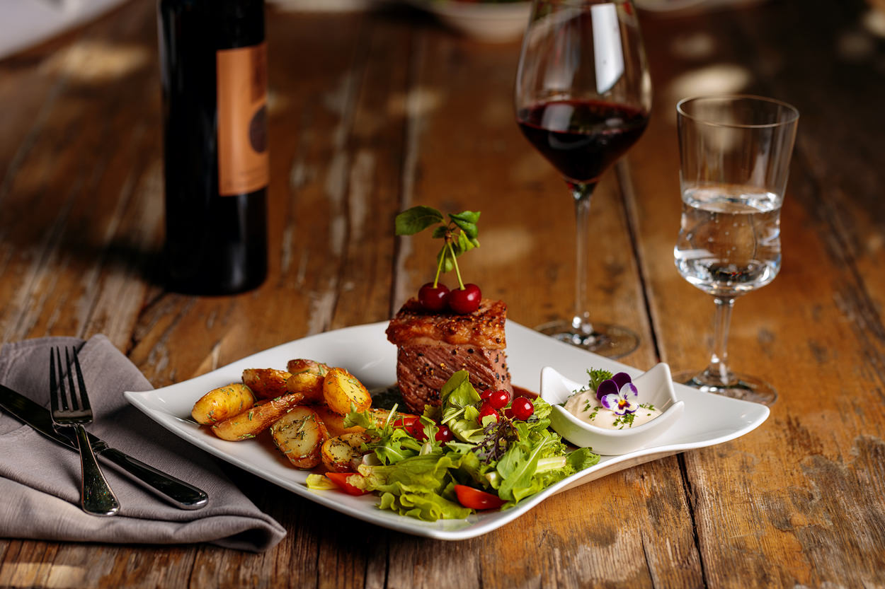 Foto von einem saftigen Steak mit Kartoffeln und Salatbeilage. Dazu ein Glas Rotwein!