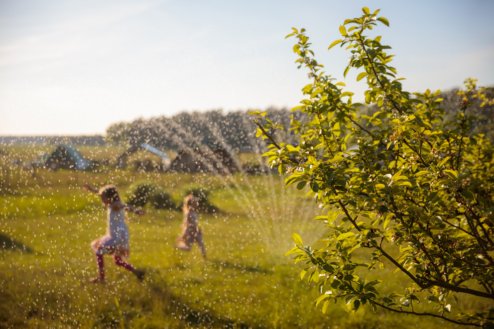 Kinder spielen im Garten von Ferienhaus mit dem Rasensprenger
