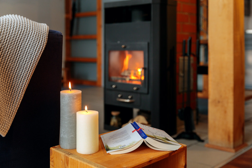 Kerzen vor Kamin mit Kuscheldecke und Buch