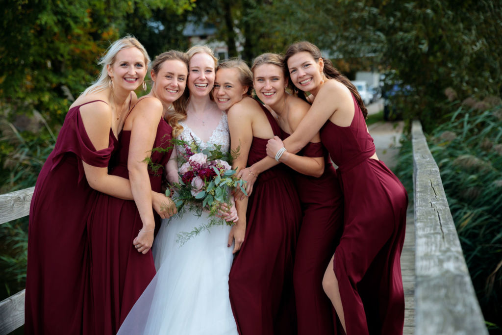 Die Braut steht mit 5 Brautjungfern, die alle das gleiche dunkelrote Kleid tragen, auf einem Steg an der Havel Die Braut steht mit 5 Brautjungfern, die alle das gleiche dunkelrote Kleid tragen, auf einem Steg an der Havel