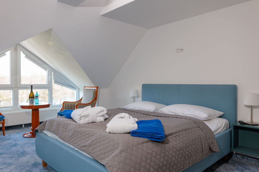 Ein gemütliches Hotelzimmer unter dem Dach mit einem großen, modern gestalteten Bett in hellem Blau.