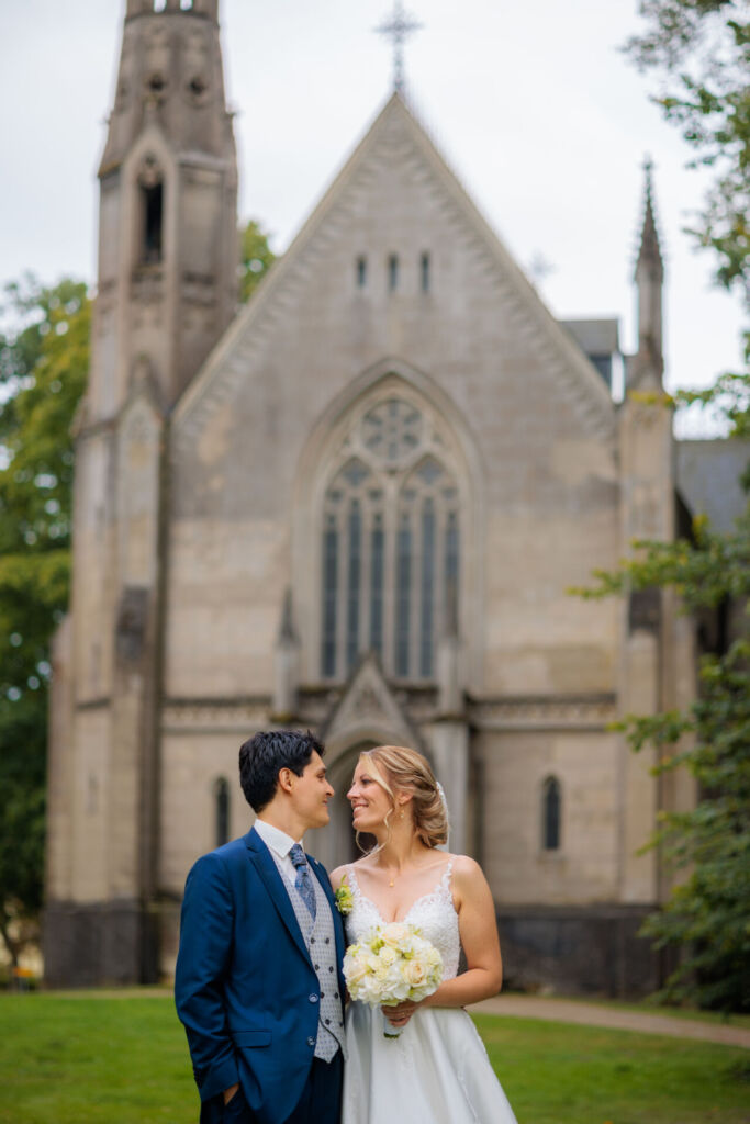 Ein frisch verheiratetes Paar steht lächelnd vor einer imposanten, historischen Kirche.