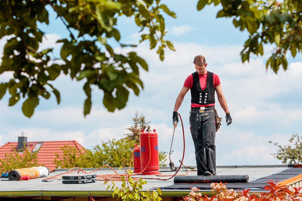 Ein Dachdecker arbeitet auf einem Flachdach unter freiem Himmel.